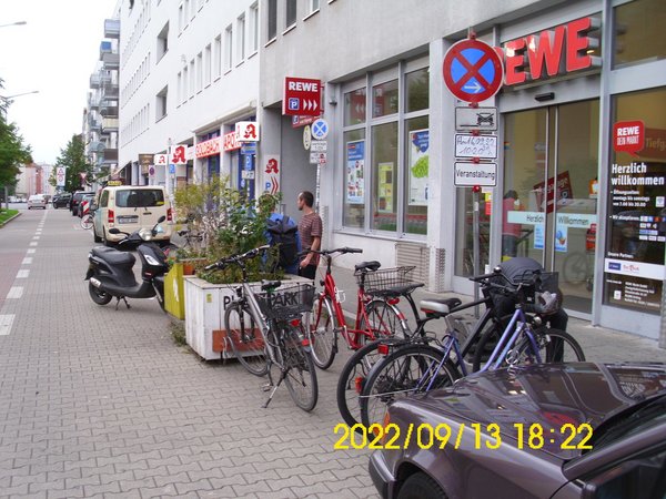 Foto mit Straßensituation vor dem REWE-Supermarkt in der Zerzabelshofstraße mit abgestellten Fahrrädern. Wie man an den aufgestellten Halteverbotsschildern erkennen kann, ist der Platz für die Veranstaltung am Park(ing)Day schon reserviert. 