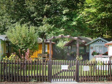 Hinter einem Holzzaun mit hölternem Toreingang eine Gruppe von sechs unterschiedlichen, liebevoll gepflegter Gartenhäuschen, das Laubenmuseum Nürnberg.