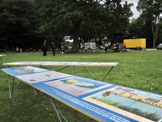 Foto: Spiegelwiese. Im Vordergrund Tische der Ausstellung, im Hintergrund unterhalten sich Besucher. 