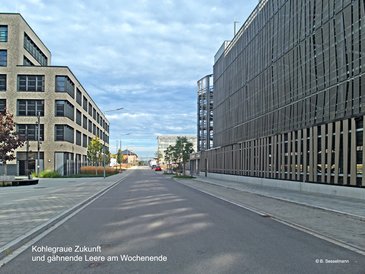 Zwischen Parkhaus und DATEV-Gebäude blickt man die Sophie-Germain-Straße entlang nach Osten; Straße, Gebäudevorplatz, Parkflächen, aber keine Menschen weit und breit.