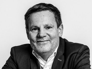 Portrait Florian Kluge, Mann im mittleren Alter, elegant gekleidet mit freundlichem aber ernstem Gesichtsausdruck 