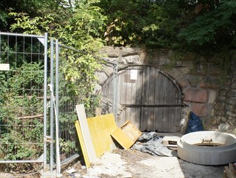 Hölzernes Eingangstor des Bierkellers in der Kellermauer des ehemaligen Lokals in der Nähe der S-Bahn Station "Reichelsdorfer Keller", davor ein Bauzaun und Baumaterialien/Abfälle.