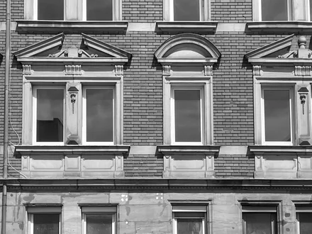 Hausfassade aus der Gründerzeit, mit gestalteten Fensterrahmen, modernen Fenstern, aber ohne Vorhänge, man sieht: das Haus steht komplett leer.