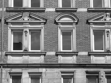 Hausfassade aus der Gründerzeit, mit gestalteten Fensterrahmen, modernen Fenstern, aber ohne Vorhänge, man sieht: das Haus steht komplett leer.
