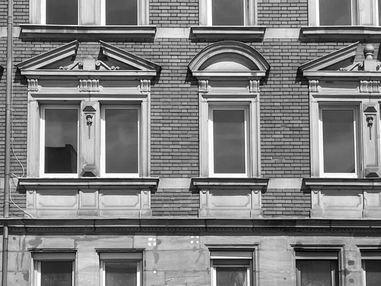 Hausfassade aus der Gründerzeit, mit gestalteten Fensterrahmen, modernen Fenstern, aber ohne Vorhänge, man sieht: das Haus steht komplett leer.