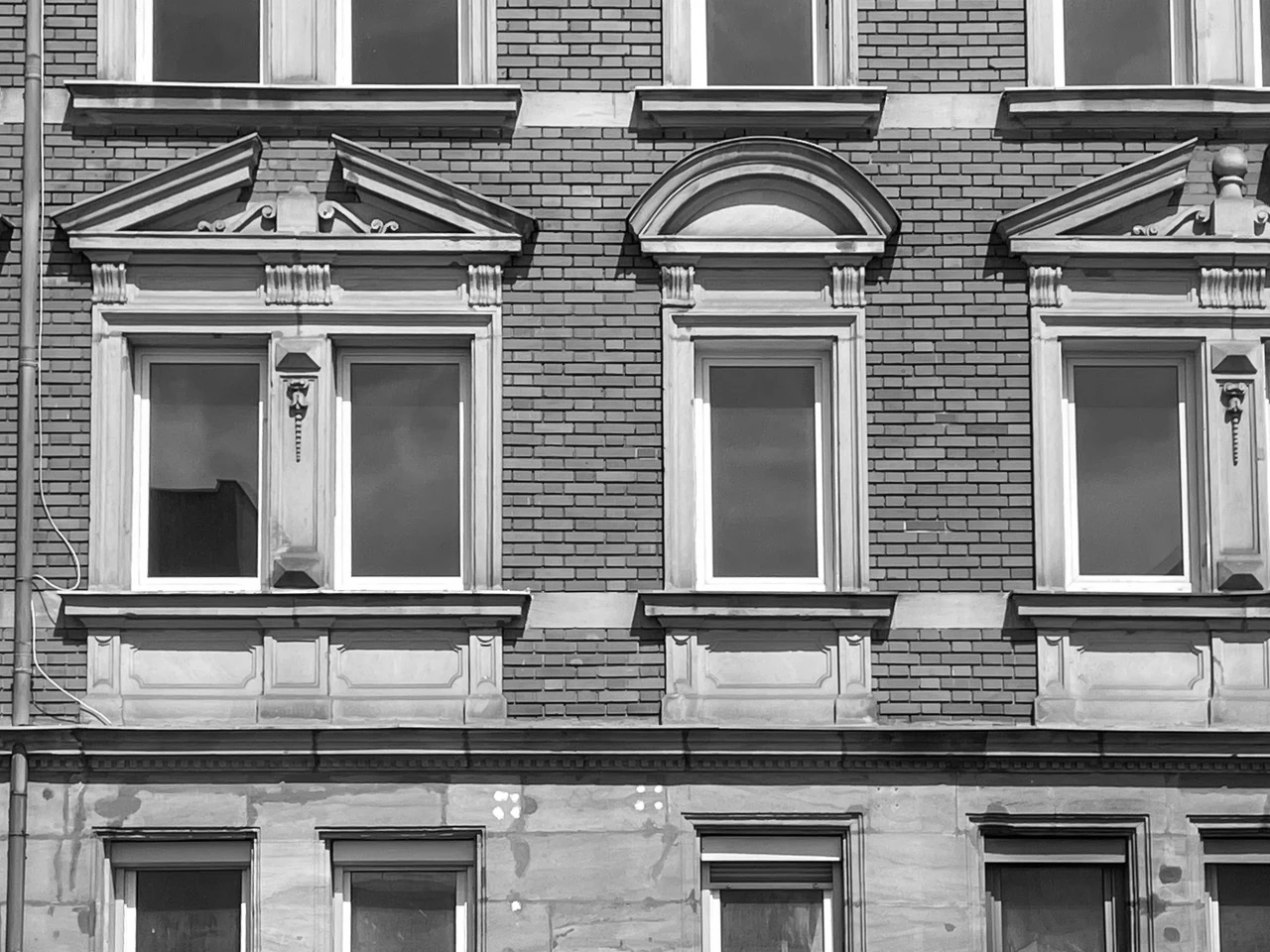 Hausfassade aus der Gründerzeit, mit gestalteten Fensterrahmen, modernen Fenstern, aber ohne Vorhänge, man sieht: das Haus steht komplett leer.